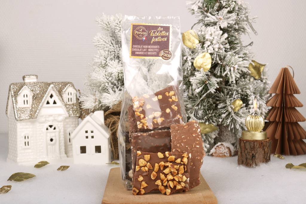 Tablettes festives mendiant au chooclat noir parsemés de raisins, amandes et noisettes et de chocolat au lait, parsemé de noisettes caramélisées, de feuillettines et d'amandes hachées.